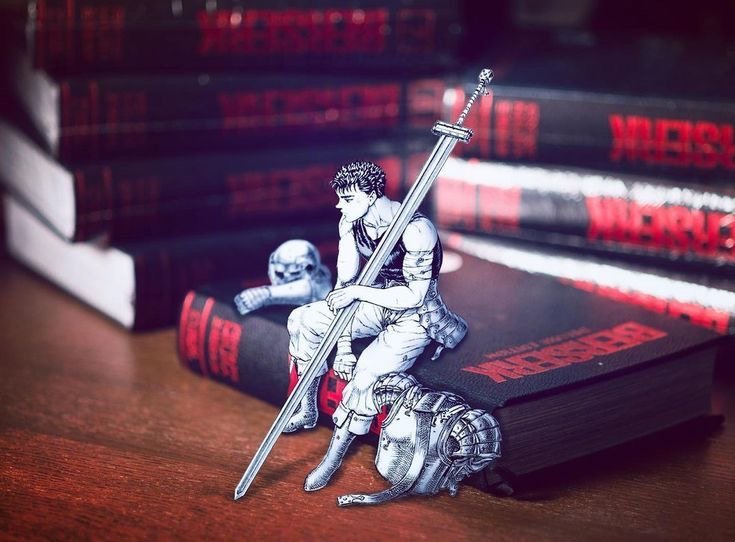 A Guts figure sitting on a stack of Berserk Deluxe Edition books